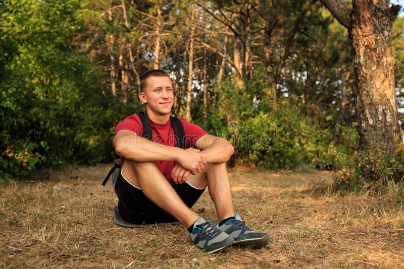 Uomo felice della viandante che si siede sulla terra e che guarda in avanti fotografia stock Uomo felice della viandante che si siede sulla terra e che guarda in avanti fotografia stock