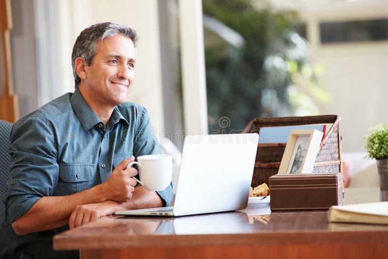 Uomo ispano maturo che per mezzo del computer portatile sullo scrittorio a casa