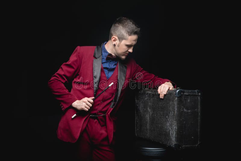 Uomo mago con bacchetta magica e valigia su fondo nero fotografia stock