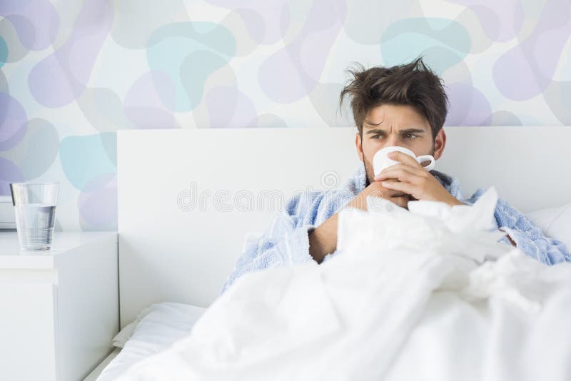 Uomo malato che mangia caffè a letto fotografia stock Uomo malato che mangia caffè a letto fotografia stock