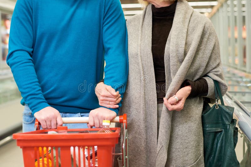 Uomo maturo che spinge il carrello della spesa mentre si sposta lungo il corridoio con la moglie fotografia stock