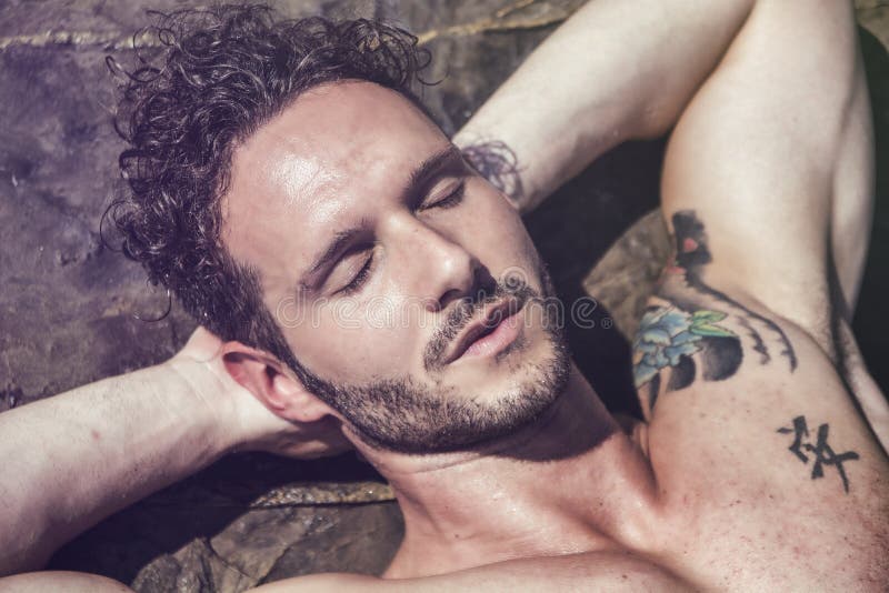 Uomo muscolare bello sulla spiaggia che mette sulle rocce immagini stock Uomo muscolare bello sulla spiaggia che mette sulle rocce immagini stock