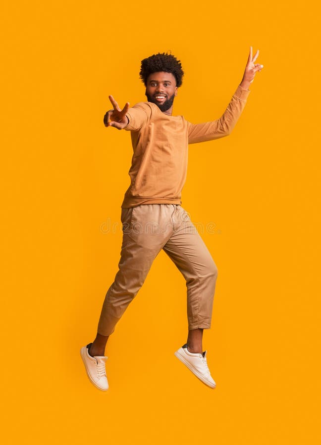 Everything is gonna be allright. Active african man gesturing peace while jumping in the air, orange background. Everything is gonna be allright. Active african man gesturing peace while jumping in the air, orange background