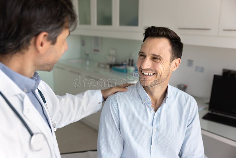 Uomo paziente allegro che riceve dal medico un gesto spalla di supporto fotografia stock
