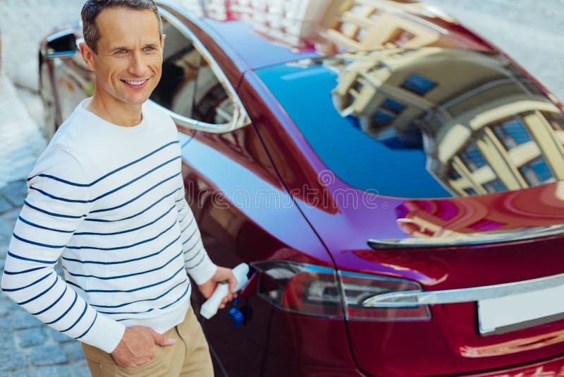 Uomo piacevole contentissimo che mette un iniettore nell'automobile immagine stock Uomo piacevole contentissimo che mette un iniettore nell'automobile immagine stock