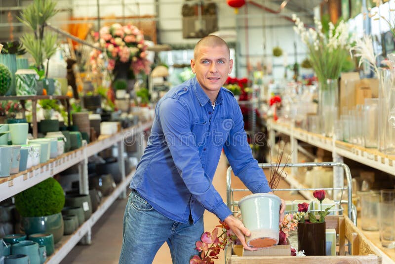 Uomo positivo che sceglie attentamente i vasi da fiore in un negozio di fiori fotografia stock libera da diritti