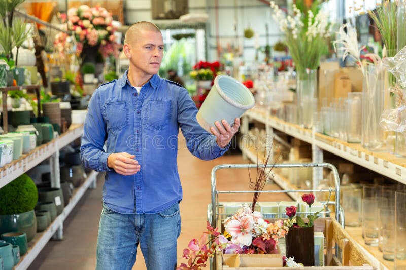 Uomo positivo che sceglie attentamente i vasi da fiore in un negozio di fiori fotografia stock