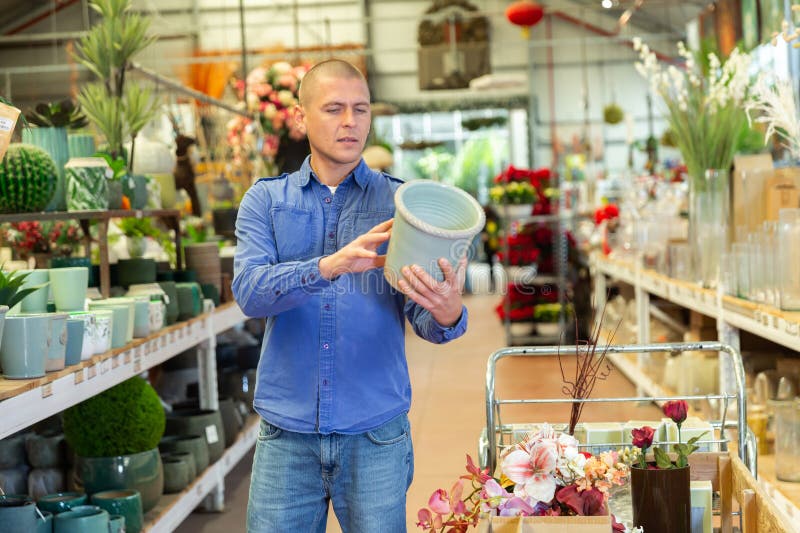 Uomo positivo che sceglie attentamente i vasi da fiore in un negozio di fiori fotografie stock
