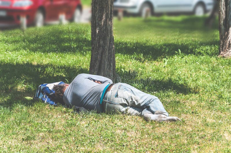 Uomo scalzo anziano del rifugiato o del senzatetto che dorme sull'erba nel parco della città facendo uso della sua borsa di viagg fotografia stock libera da diritti Uomo scalzo anziano del rifugiato o del senzatetto che dorme sull'erba nel parco della città facendo uso della sua borsa di viagg fotografia stock libera da diritti