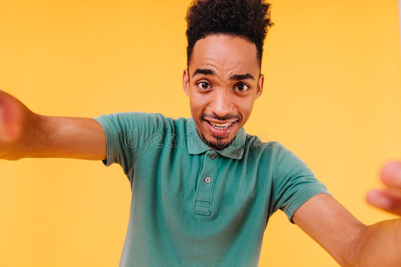 Uomo scuro di buon umore con capelli corti che si fa selfie. foto di un ragazzo africano in verde all'interno immagini stock
