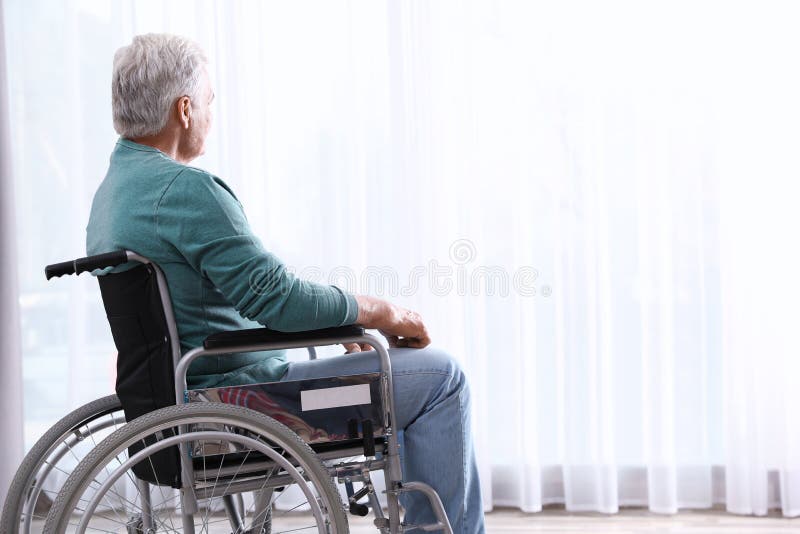 Uomo senior che si siede in sedia a rotelle vicino alla finestra fotografia stock libera da diritti Uomo senior che si siede in sedia a rotelle vicino alla finestra fotografia stock libera da diritti