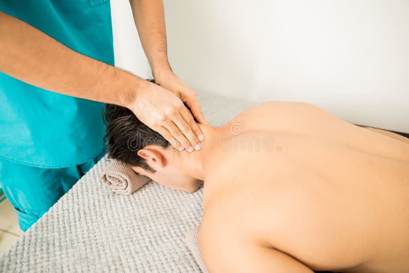 Uomo senza camicia che riceve massaggio del collo dal terapista In Hospital immagini stock libere da diritti Uomo senza camicia che riceve massaggio del collo dal terapista In Hospital immagini stock libere da diritti