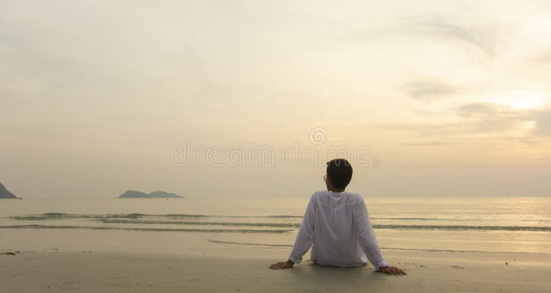 Uomo solo seduto sulla spiaggia e che guarda il cielo al tramonto immagine stock