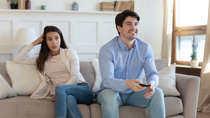 Smiling men watching tv show, football or soccer match, bored angry women sitting on couch separately at home, young couple disagreement and misunderstanding, channel choice problem concept. Smiling men watching tv show, football or soccer match, bored angry women sitting on couch separately at home, young couple disagreement and misunderstanding, channel choice problem concept