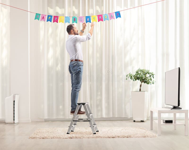 Uomo su una scala che appende decorazioni di compleanno fotografie stock