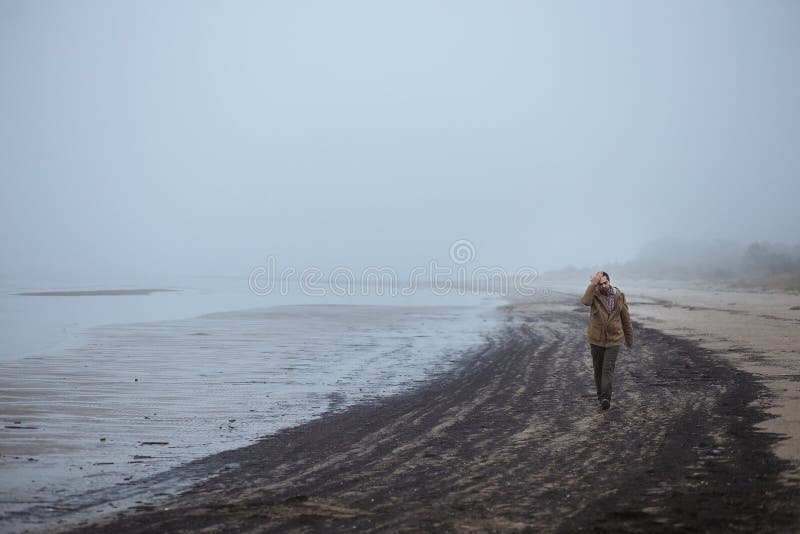 Uomo triste solo che cammina su una spiaggia nebbiosa immagini stock libere da diritti Uomo triste solo che cammina su una spiaggia nebbiosa immagini stock libere da diritti