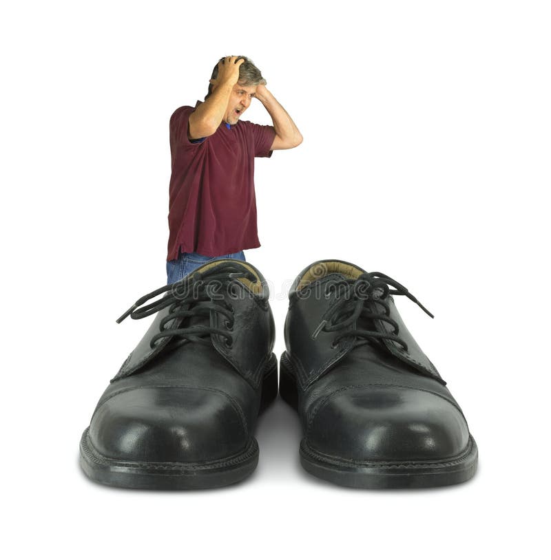 Uomo turbato che sta davanti ad alcune grandi scarpe per riempire fotografia stock Uomo turbato che sta davanti ad alcune grandi scarpe per riempire fotografia stock