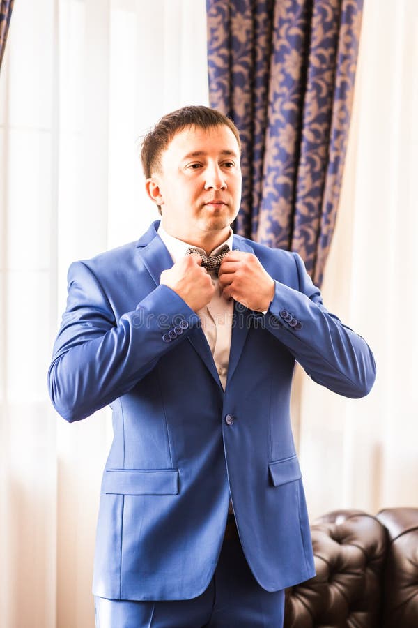Uomo in vestito blu che regola il suo farfallino mentre stando contro lo specchio immagine stock libera da diritti Uomo in vestito blu che regola il suo farfallino mentre stando contro lo specchio immagine stock libera da diritti