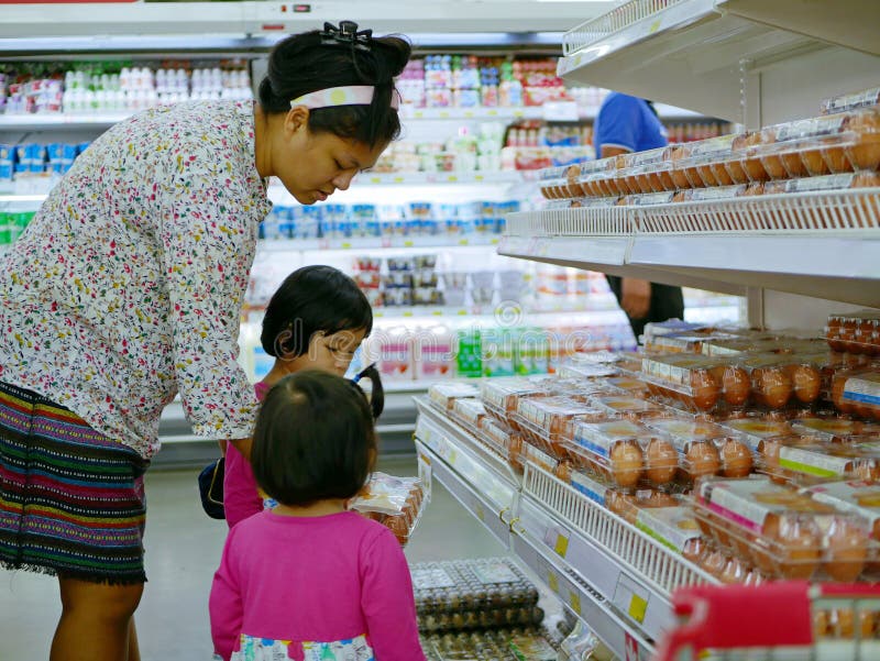 Uova che asiatiche del pollo di rappresentazione della madre vuole comprare alle sue due piccole figlie ad un supermercato fotografia stock libera da diritti Uova che asiatiche del pollo di rappresentazione della madre vuole comprare alle sue due piccole figlie ad un supermercato fotografia stock libera da diritti