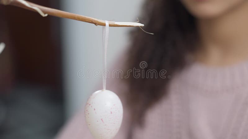 Uova decorative di pasqua appese a mano da ragazza su un ramo. adolescente afro-americano irriconoscibile