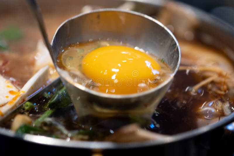 Close up of raw egg in soup ladle put into a sukiyaki pot. Close up of raw egg in soup ladle put into a sukiyaki pot