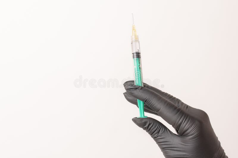 Hand in black glove with a filled syringe with a needle on a white, isolated background. Ready for injection medicine, drugs, vaccine or steroids. Copy, free space. Hand in black glove with a filled syringe with a needle on a white, isolated background. Ready for injection medicine, drugs, vaccine or steroids. Copy, free space.