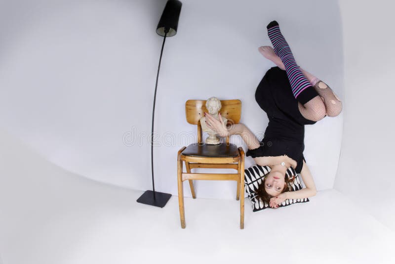 A teen age girl up side down seating on a pillow isolated on white. A teen age girl up side down seating on a pillow isolated on white