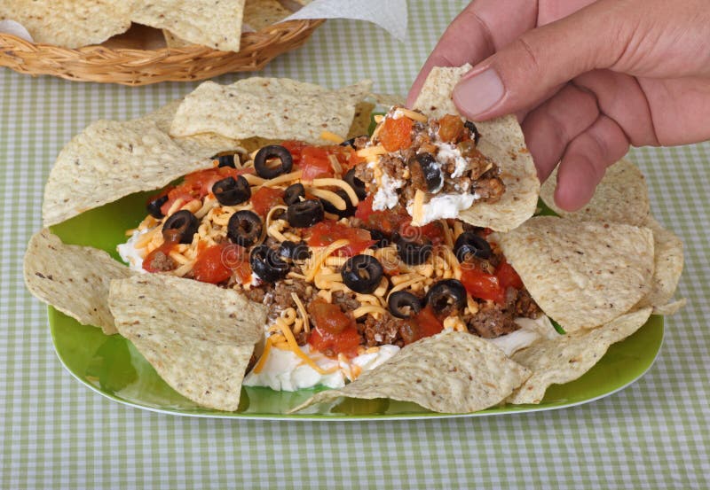 Taco dip consisting of hamburger, cheese, black olives, and tomatoes with tortilla chips. Taco dip consisting of hamburger, cheese, black olives, and tomatoes with tortilla chips