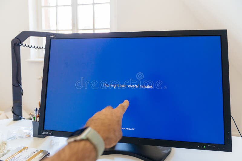 Paris, France - Sep 7, 2020: POV male hand pointing to large Nec Spectraview Reference monitor showcasing THis might take several minutes text during Microsoft Windows blue screen update.