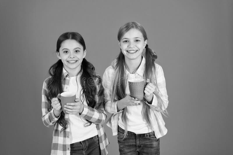 Make sure kids drink enough water. Girls kids hold cups orange background. Sisters hold mugs. Drinking tea while break. Relaxing with drink. Tea break. Children do not drink enough during school day. Make sure kids drink enough water. Girls kids hold cups orange background. Sisters hold mugs. Drinking tea while break. Relaxing with drink. Tea break. Children do not drink enough during school day.