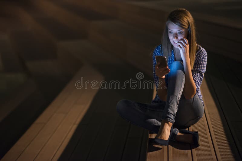 Upphetsad härlig flicka som mottar ett smsmeddelande med goda nyheter i en mobiltelefon utanför royaltyfri bild Upphetsad härlig flicka som mottar ett smsmeddelande med goda nyheter i en mobiltelefon utanför royaltyfri bild