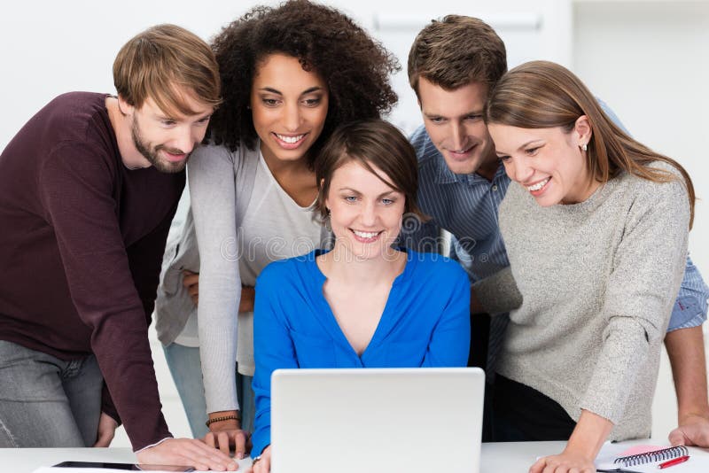 Excited young business team grouped together looking at a laptop as they review their latest presentation together smiling in satisfaction. Excited young business team grouped together looking at a laptop as they review their latest presentation together smiling in satisfaction