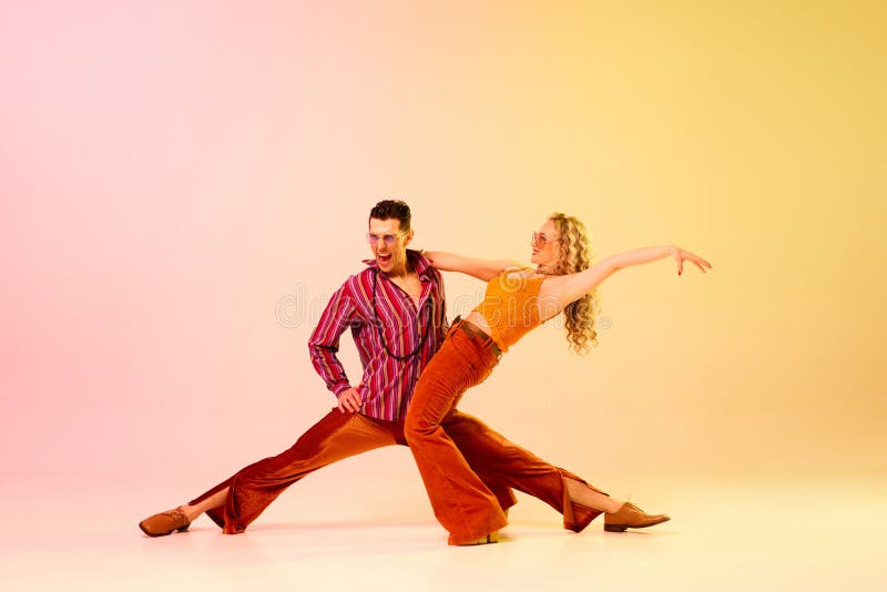 Upphetsning. konstnärligt uttryckligt par man och kvinna som emotionellt dansar discodans mot gradient rosa gul royaltyfri fotografi