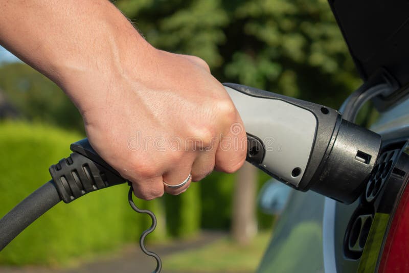 Eletric car charging in summer closeup photo with male hand. Green background. Eletric car charging in summer closeup photo with male hand. Green background.