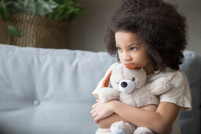 Upset lonely bullied little african american kid girl holding teddy bear looking away feels abandoned abused, sad alone preschool mixed race child orphan hugging stuffed toy, charity adoption concept. Upset lonely bullied little african american kid girl holding teddy bear looking away feels abandoned abused, sad alone preschool mixed race child orphan hugging stuffed toy, charity adoption concept