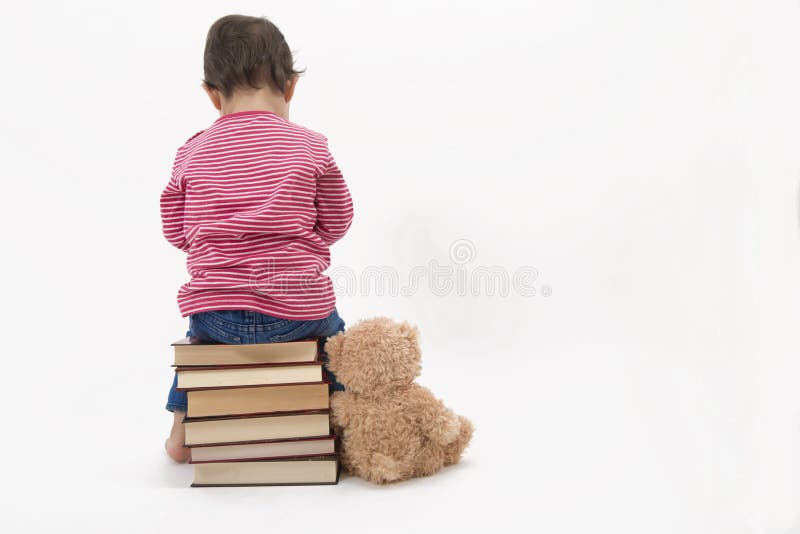 Upprivet barnsammanträde på böcker med henne som är teddybear arkivbilder Upprivet barnsammanträde på böcker med henne som är teddybear arkivbilder
