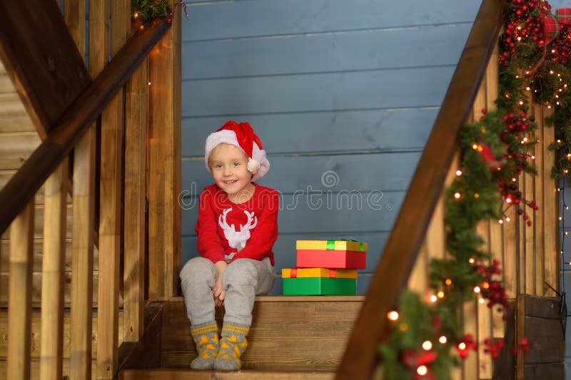 Uppspelad liten pojke med en julklapp på trapphus i huset. porträtt av lyckligt barn i julmorgon arkivbild