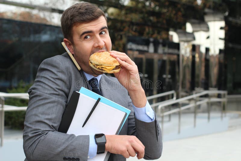 Upptagen affärsman som samtidigt går, kallar och har lunch arkivfoto Upptagen affärsman som samtidigt går, kallar och har lunch arkivfoto