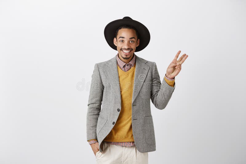 Uppvisning av av tre vägar eller val Studioskottet av den nöjda lyckade afrikanska pojkvännen i stilfull hatt och grå färger klår arkivfoton Uppvisning av av tre vägar eller val Studioskottet av den nöjda lyckade afrikanska pojkvännen i stilfull hatt och grå färger klår arkivfoton