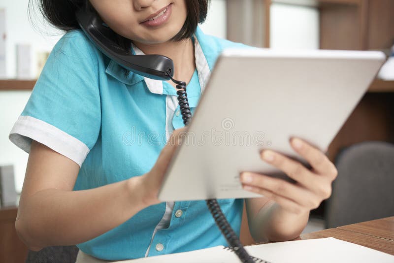 Uprawa salonu administrator używa pastylkę i mówienie na telefonie. Współczesna młoda kobieta na recepcyjnej używa pastylce podczas gdy mówjący z klientem na telefonie