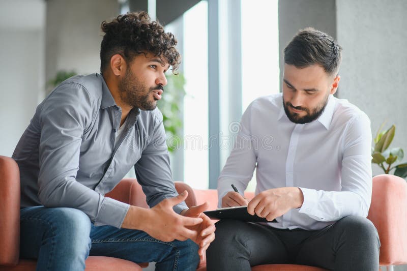 Upset arab man discussing problems with psychologist taking notes during therapy session royalty free stock photo