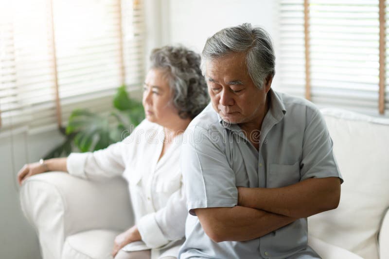 Upset Senior man sitting on sofa against the background of his wife