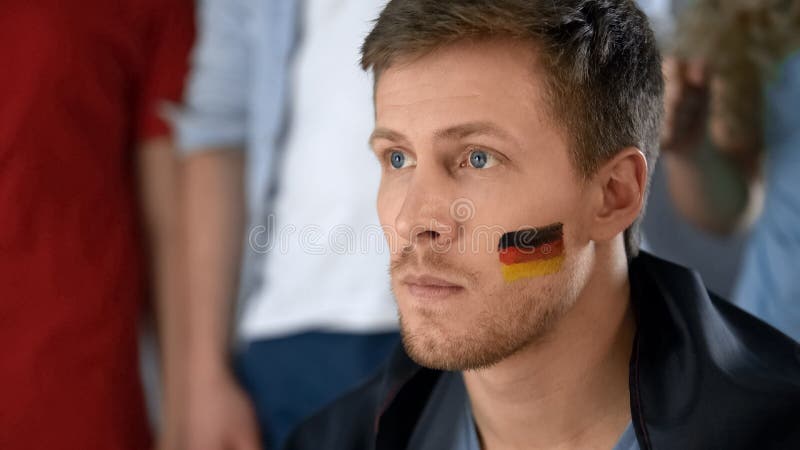 Upset German football fan disappointed with defeat, watching game with friends royalty free stock photography Upset German football fan disappointed with defeat, watching game with friends royalty free stock photography