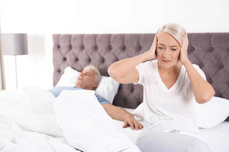 Upset mature woman sitting on bed near her sleeping husband at home. royalty free stock photography Upset mature woman sitting on bed near her sleeping husband at home. royalty free stock photography
