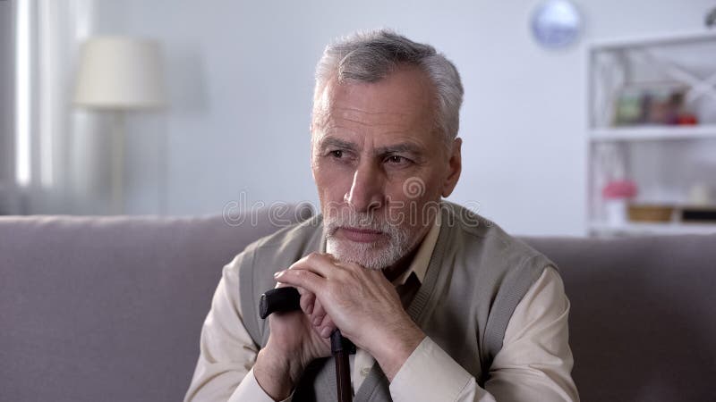 Upset old man with walking stick sitting on coach and thinking of difficult life, stock photo