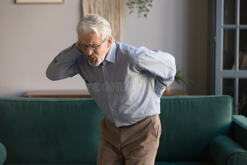 Upset senior man feeling back pain injury standing at home stock image Upset senior man feeling back pain injury standing at home stock image