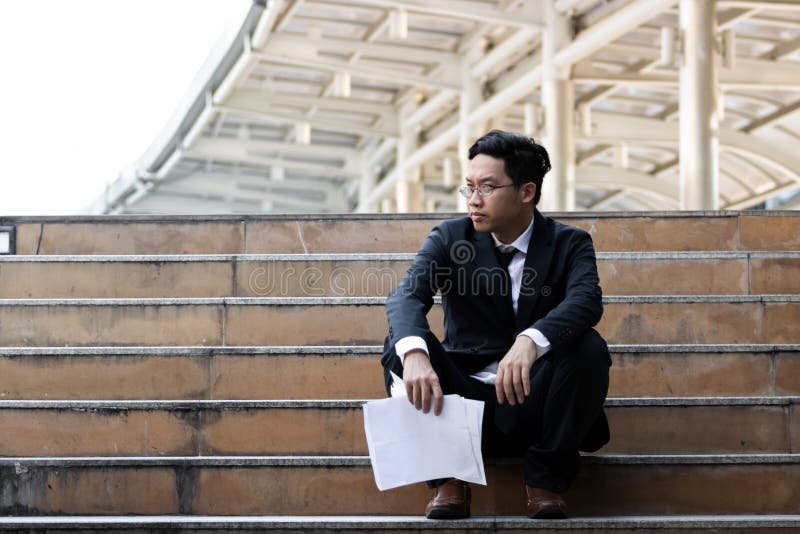 Upset stressed young Asian business man sitting on stairs and suffering from severe depression. Unemployment and layoff concept. stock photos Upset stressed young Asian business man sitting on stairs and suffering from severe depression. Unemployment and layoff concept. stock photos