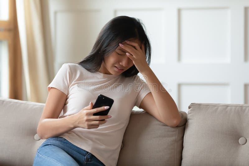 Upset young Asian woman crying, holding phone, received bad message