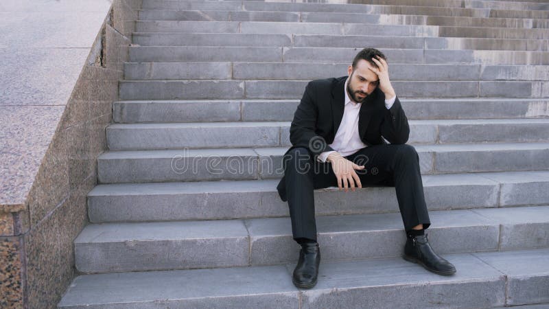 Upset young business man having stress and sitting on stairs in street. Businessman having deal problems concept royalty free stock photography Upset young business man having stress and sitting on stairs in street. Businessman having deal problems concept royalty free stock photography