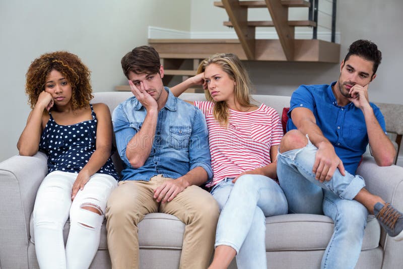 Upset young friends sitting on sofa at home
